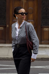 a lady in a white ruffle collared shirt, a grey sweater and a pair of black pants